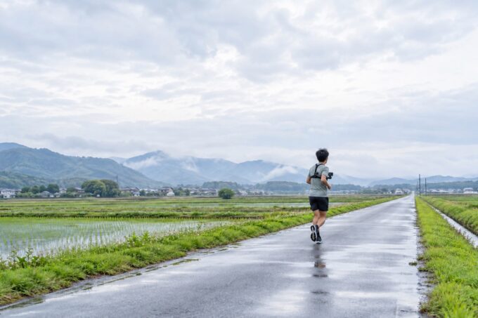 胸元にカメラを付けて田園の道を走るランナーの後ろ姿